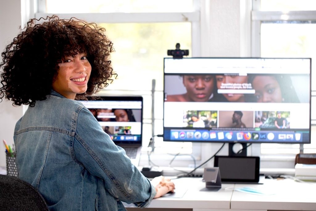 A brown girl working at her desk on her computer and looking over her right shoulder.