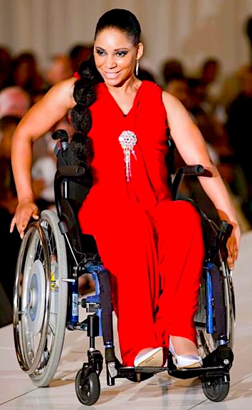 A black woman with light skin in a wheelchair on stage, wearing a red outfit.