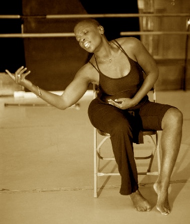 A black female dancer sits in a chair and strikes a pose.