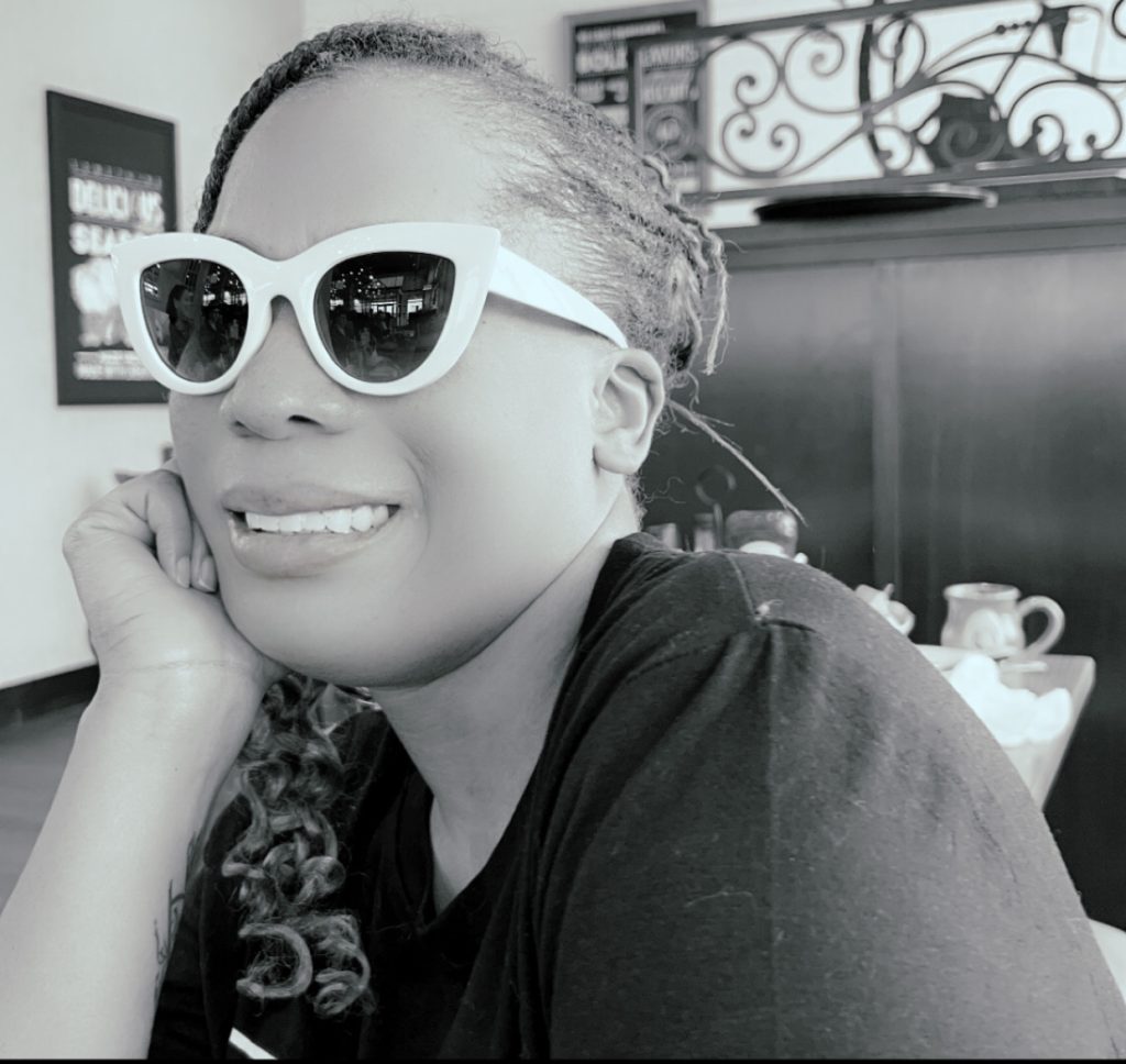 Black and white photo of the author wearing white-rimmed glasses and smiling.