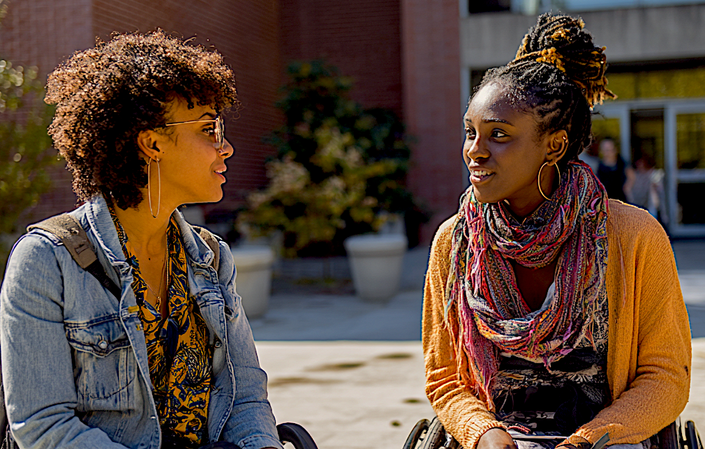 An older black woman in a wheelchair mentoring a younger black woman in a wheelchair. Image produced using Midjourney